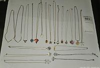 Wide view of 17 vintage necklaces on white background showing diverse pendant shapes and chain styles including heart, leaf, flower, star, and shell designs