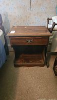 Front view of vintage wooden night stand showing drawer with brass handle and open lower shelf. Top surface has visible damage and wear.