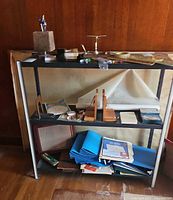 Shelving unit with assorted office supplies, drafting tools, rulers, folders, and organizers spread across three shelves