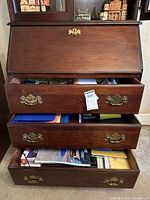 Front view of wooden chest with open drawers showing contents of office supplies and maps inside