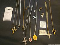 Full view of all religious jewelry items including necklaces, crosses, charms, and clip-on earrings arranged on black background.