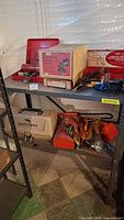 Shelf display of multiple tools including Craftsman sander in box on top shelf, several hand tools, and red toolbox with items inside on bottom shelf.