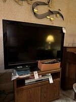 Front view of Sony Bravia 40-inch TV on wooden stand with remotes and cords in a box in front