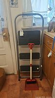 Step ladder standing upright showing full view with mini broom and dustpan in front.