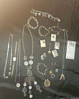 Full lot of sterling silver and silver tone bracelets, necklaces, charms, pins, clip earrings, and Armitron watch displayed on black fabric.
