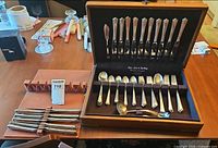Wooden box open on table showing flatware in velvet insert and separate wooden rack with steak knives