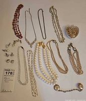 Full lot showing various vintage necklaces mostly with faux pearls, metal chains, a sweater clip rhinestone piece missing one stone, a container of loose faux pearls, and an assortment of non-pierced clip-on earrings in rhinestone and gold tone.