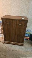 Closed cabinet with two vertical doors, dark wood finish, metal handles, and a lock without key, placed on carpeted floor.