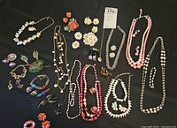 Top view of all jewelry sets spread out on black surface showing variety of necklaces, earrings, pins, and bracelets in multiple colors and designs.