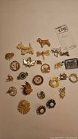 Top-down image showing multiple vintage pins laid out including dog shapes, floral motifs, abstract circular designs, and a small rectangular house scene pin.