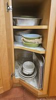 Cabinet shelf showing stacked white dishes, clear glass bowls, and aluminum trays