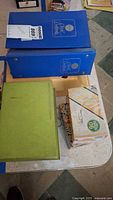 Top view of two blue binders, one green binder, and one box of recipe cards on table