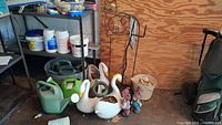 Overview showing four plastic watering cans, three swan-shaped plastic planters, metal decorative yard hooks, and a plastic bucket with garden statues