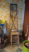 Full view of all three wooden ladders grouped together inside a room with vintage wallpaper background. One ladder stands about 6 feet tall with two smaller step ladders in front.