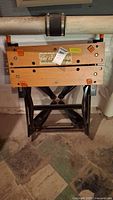 Black and Decker Workmate folding work table upright, showing wooden top and black metal legs in basement setting.