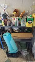 Photo showing multiple plastic planters, gardening chemicals including Miracle-Gro and Miracid containers, spray bottles, blue rolled mat, and various pots arranged on metal shelving units.