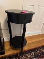 Full view of black wooden round side table with curved legs and lower shelf.