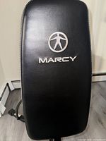 Close-up of the black padded seat backrest with Marcy logo embroidered in silver.