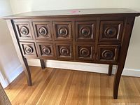 Front view of the wooden side table showing the 10 drawers with circular carved handles and the slightly curved legs.