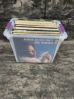 Plastic storage box filled with old vinyl records, showing the front album cover of Hawaii Beach Party by The Waikikis.