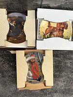 Three decorative collector plates still in original cardboard packaging, showing distinct artwork on each plate including a man with violin, a dog, and a child.