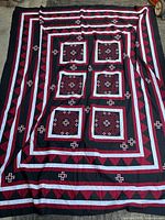 Full view of the handmade quilt showing central red diamond motifs within square frames and borders of red, black, and white geometric patterns.