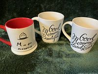 Photo of three coffee mugs with various text designs, showing shape, handles, and color variation on interior.