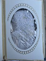 Front view of the folded white wedding gown inside the original Keepsafe Pak box with open top and clear window.