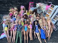 Photo showing a group of about 30 Barbie dolls with varied appearances and outfits. Also includes a toy unicorn and miniature supermarket shelves.