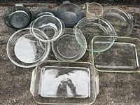 Cluster of 11 clear glass Pyrex dishes in assorted shapes and sizes on ground, showing overall lot contents.