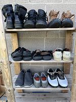 Photo showing three shelves with various men's shoes arranged on them including boots, sandals, sneakers, and casual shoes.