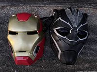 Photo showing two Marvel superhero face masks: Iron Man mask in metallic gold and red, Black Panther mask in black with silver accents and raised patterned detailing.