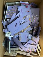 Top-down photo of a box filled with new Claire’s jewelry on original cards including earrings, bracelets, and necklaces in mixed styles and colors.
