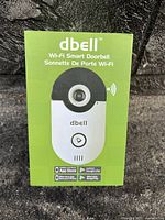 Front view of unopened green retail box showing dbell Wi-Fi Smart Doorbell image and app compatibility logos.