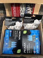 Photo of two boxes of Noma C9 Blue LED string lights and one box of 25 Noma C9 Quick-Clip light clips/holders inside an open cardboard box.