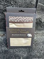 Photo of the two-pack satin pillowcase set in original packaging showing cream and patterned flap design with text on packaging.