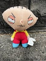 Front-facing image of Stewie Griffin plush toy showing facial detail, clothing colors, and attached tag.