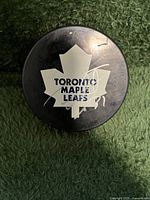 Front side of the hockey puck displaying the Toronto Maple Leafs maple leaf logo with one autograph in silver marker.