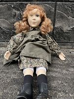 Full view of the vintage Anne of Green Gables doll sitting against a stone background. Shows the doll's dress, apron, boots, and curly hair.