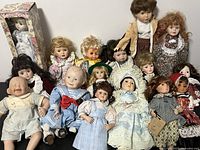 Large assortment of vintage porcelain dolls of various sizes and attire grouped together on a surface.