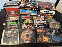 Photo of multiple vintage PC game CDs, various titles from the 1990s and early 2000s visible, stacked and arranged on a white surface.