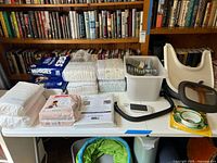 Overview of baby diapers, baby monitor device and parts, feeding set, hangers, blackout curtains, tape, and accessories on white table