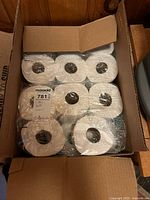 Open top view of a cardboard box showing plastic wrapped packs of white bath tissue rolls inside.