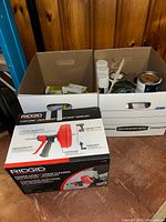 Ridgid Power Spin drain cleaner boxed and two boxes containing assorted light switches and wall plates