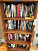 Wooden bookshelf showing two upper shelves filled with assorted hardcover books in dust jackets