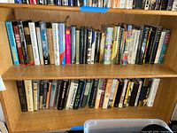 Books arranged on oak shelves showing a large collection of novels and non-fiction titles in hardcover and paperback formats.