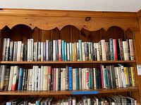 Two wooden shelves filled with rows of hardcover books showing spines and dust jackets
