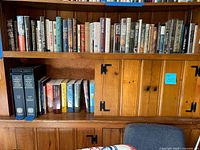 Wide view of wooden bookshelf with assorted hardcover and paperback books including mystery and literary fiction titles.