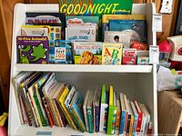 Photo of a white bookshelf filled with colorful children's books including titles 'Goodnight Moon', 'Hi-Five Animals!', 'ABC Read to Me: NYC', 'First 100 Animals' and more. Books are a mix of board and story books.