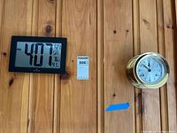 Marathon digital clock and brass maritime clock mounted on wood paneling, showing the lot contents.